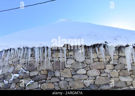 Altes schneebedecktes Palloza Rundsteinhaus mit Reetdach und Eiszapfen. Piornedo-Bergdorf, Ancares, Lugo, Galicien, Spanien. Stockfoto