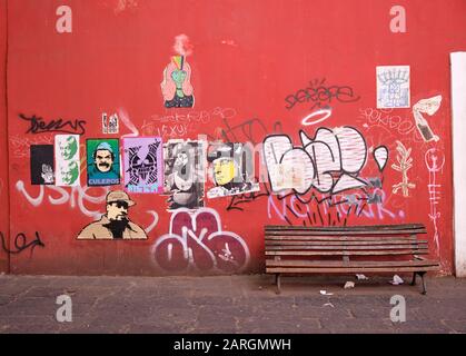 Rote Wand in der kolonialen Altstadt von Puebla mit verschiedenen Dekal-Kunstplakaten und Graffiti mit leerer Holzbank bedeckt Stockfoto