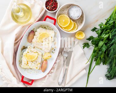 Kabeljaufischfilet, frisch im Ofen mit Zwiebel in Porzellanform zum Backen, Zitrone auf Platte, Draufsicht Stockfoto