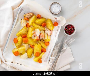 Buntes geröstetes Gemüse auf dem Tablett mit Pergament. Kartoffeln, Karotten und Zwiebeln. Heller Marmortisch. Draufsicht Stockfoto