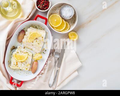 Kabeljaufischfilet, frisch im Ofen mit Zwiebel in roter Porzellanform zum Backen, Zitrone, Draufsicht, Kopierraum Stockfoto