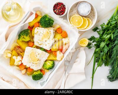 Fisch-Kabeljau im Ofen mit Gemüse gebacken - gesunde Ernährung gesundes Essen. Hellweißer Marmortisch, Kopierraum, Draufsicht Stockfoto