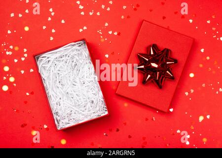 Eine geöffnete Geschenkbox mit Schleife, in die Sie ganz einfach jedes Objekt legen können. Roter festlicher Hintergrund mit Herzen. Frohe Weihnachten, Valentinstag, Alles Gute Zum Geburtstag und andere Feiertage. Stockfoto