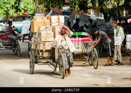 Güter und große Lasten werden mit menschlicher Kraft auf Karren transportiert und Fahrradrickshaws auf der Khari Baoli Road in Old Delhi gefahren Stockfoto