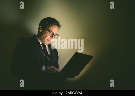 Porträt eines gutaussehenden persischen Geschäftsmannes, der Laptop im dunklen Raum verwendet Stockfoto