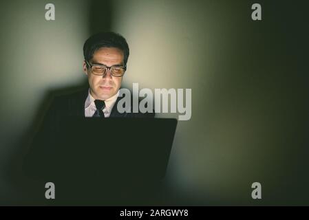 Porträt eines gutaussehenden persischen Geschäftsmannes, der Laptop im dunklen Raum verwendet Stockfoto