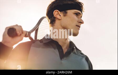 Nahaufnahme eines professionellen Tennisspielers, der an einem sonnigen Tag draußen steht. Männliche Tennisspielerin mit Racket Looking Away. Stockfoto