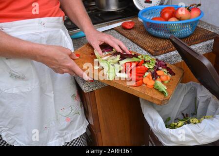 Detail einer weiblichen Hand Entsorgung der organischen Abfälle in einem geeigneten Behälter mit Küche im Hintergrund Stockfoto