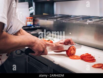 Nahaufnahme des Kochs. In einer professionellen Küche schneiden Küchenchef frische Tomaten. Gemüse für Burger zubereiten. Fast Food Küche Stockfoto