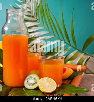 Zwei Gläser und eine Flasche tropisch exotischer Multifruchtsaft mit Ananas und Palmblatt im Hintergrund. Stockfoto