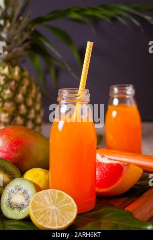 Zwei Flaschen tropisch exotischer Multifruchtsaft unter Palmblättern mit Früchten im Hintergrund Stockfoto