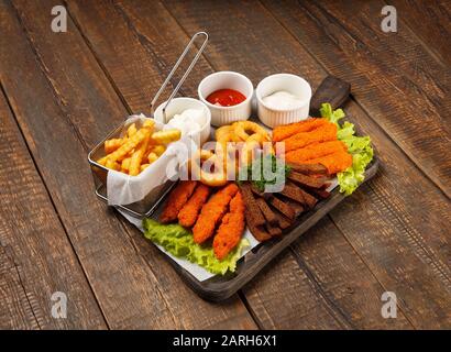 Bier-Snacks in der Nähe. Gegrillter Käse, Nuggets, Zwiebelringe und Soßen auf Holzgrund. Stockfoto