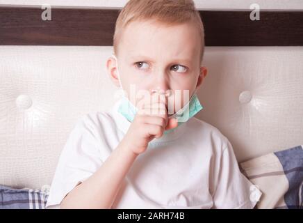Kranke Junge in einer medizinischen Maske Leiden von Husten im Bett zu Hause. Stockfoto