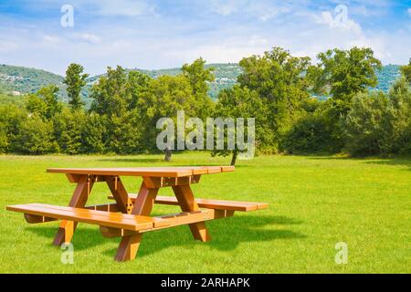 Holz- Tisch für Picknick auf der grünen Wiese in einem öffentlichen Park mit Bäumen auf Hintergrund und klaren Himmel. Stockfoto