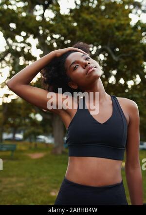 Porträt einer jungen afroamerikanischen Frau, die sich während des Trainings im Park den Hals streckte Stockfoto