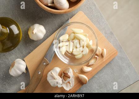 Schüssel mit Knoblauchscheiben, Birnen, Öl, Messer, Brett auf grauem Holzhintergrund. Draufsicht Stockfoto