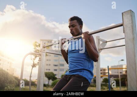 Ein afroamerikanischer junger Fit Mann, der im Freien an der horizontalen Bar Pull-ups macht Stockfoto