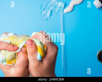 Auf blauem Untergrund mit orangefarbener Farbe. Kinder Hände halten Schleim. Bildung und modernes Spielzeugkonzept Stockfoto