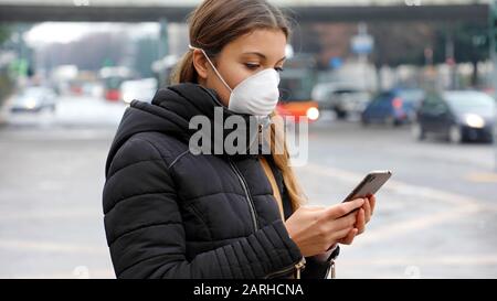 COVID-19 Pandemic Coronavirus Junge Frau mit Smartphone in der Stadt Straße trägt Gesichtsmaske wegen Covid-19, Luftverschmutzung, Partikel, Grippe Vir Stockfoto