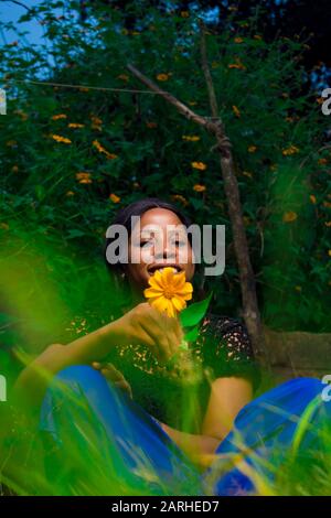 Junge afrikanerin, die allein in einem Garten eine Baummarigold-Blume hält Stockfoto