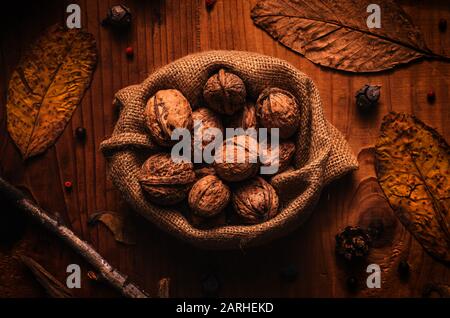 Blick auf die Walnüsse mit Schalen in umweltfreundlichem Burlap Sack auf rustikalem Holztisch mit trockenen Herbstblättern und Ästen Stockfoto