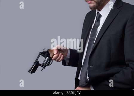 Das Porträt eines bärtigen Mannes in einem Business-Anzug hält einen Revolver in der Hand und lädt ihn wieder ein. Auf grauem Hintergrund. Krimineller Typ Mann, Gangster, Mörder, bu Stockfoto