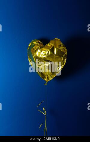 Golden Heart Shaped Airballon auf blauem Hintergrund mit Copyspace. Zerknautschter Ballon. Liebe und Valentinstag Konzept. Stock-Foto. Stockfoto