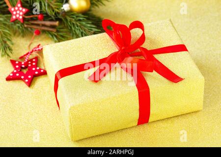 Handgefertigtes weihnachtsgeschenkkarton. Weihnachten präsentiert goldenen Kasten mit rotem Band und Baumzweig. Stockfoto