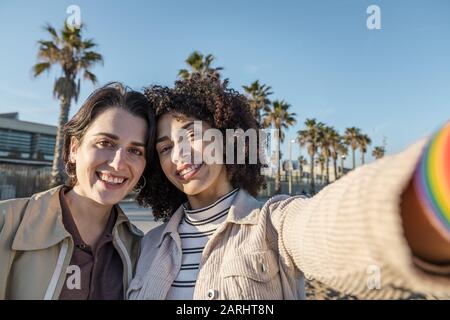 Selfie Foto des jungen interracial Paares schöner Mädchen in einer Palme und blauem Himmel Hintergrund, Konzept der weiblichen Freundschaft und Rassenvielfalt Stockfoto