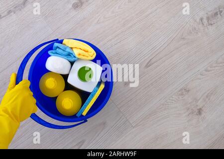 Waschmittel in Kunststoffflaschen, Schwämmen, Bürste in blauem Haushaltsbecher. Hand in gelbem Gummihandschuh. Сleaning Zubehör. Flaches Lay. Kopierbereich. Stockfoto