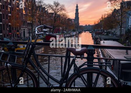 Abend über den schönen Grachten von Amsterdam im späten Herbst. Fahrräder parkten an den Brücken im Vordergrund und booten im Kanal Stockfoto