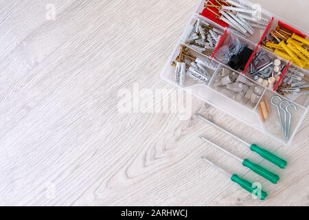 Werkzeugkasten mit Schrauben, verschiedenen Teilen und Schraubendrehern auf hellem Holzhintergrund. Machen Sie es sich selbst. Reparaturkonzept. Flaches Lay. Kopierbereich. Stockfoto