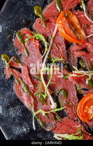 Carpaccio aus Rindfleisch mit Pesto und Tomaten auf schwarzem Tisch. Restaurant-Menü, natürliches und organisches Speisekonzept. Stockfoto