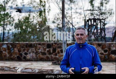 Vorderansicht des alten Mannes, der während des Stehens gegen Bäume im Park Drohne fliegt, Fokus auf den alten Mann Stockfoto