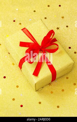 Handgefertigtes Weihnachtsgeschenkkarton mit goldenem Hintergrund. Weihnachten präsentiert goldenen Kasten mit rotem Band. Stockfoto
