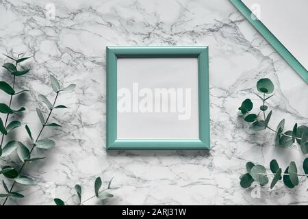 Flaches Lay, Eukalyptus von oben auf marmornem Hintergrund, helle, strukturierte Tischfläche aus Stein. Trendiger Hintergrund mit Kopierfläche in grünem quadratischem Holzrahmen Stockfoto