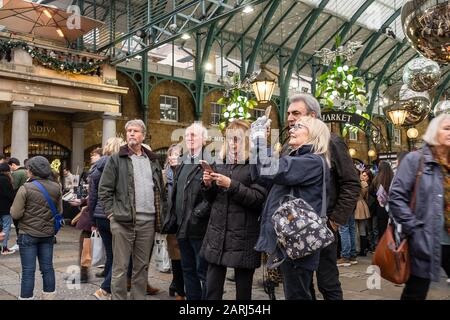 London/Großbritannien - 24. November 2019: Ältere Touristen fotografieren Weihnachtsdekorationen auf dem Apple-Markt in Covent Garden, London, Großbritannien (Selective Focus) Stockfoto