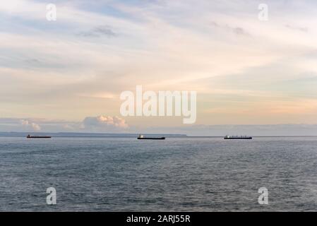 Leere Frachtschiffe ankerten am Horizont außerhalb der Küste von Lissabon an ruhiger Sonneneinstrahlung am Nachmittag Stockfoto