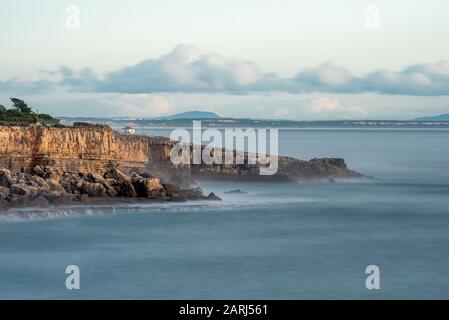 Die Klippen und der Atlantische Ozean im Wahrzeichen Boca do Inferno in Cascais Portugal in der Nachmittagssonne mit glattem Meer, das auf Felsen mit langer Belichtung abstürzt Stockfoto