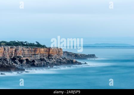 Die Klippen und der Atlantische Ozean im Wahrzeichen Boca do Inferno in Cascais Portugal in der Nachmittagssonne mit glattem Meer, das auf Felsen mit langer Belichtung abstürzt Stockfoto