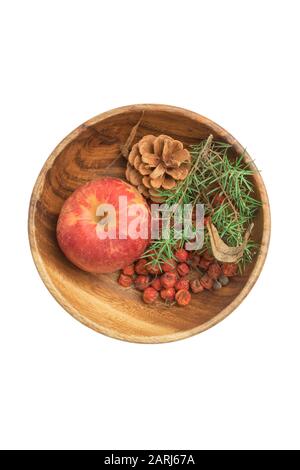 Herbststillleben: Viel reife, rowanische Beeren, Kiefernkegel, Reife trockene Vogel-Kirschbeeren, stacheliger, grüner Wacholder und heller, roter Apfel in Holzschüssel. Stockfoto