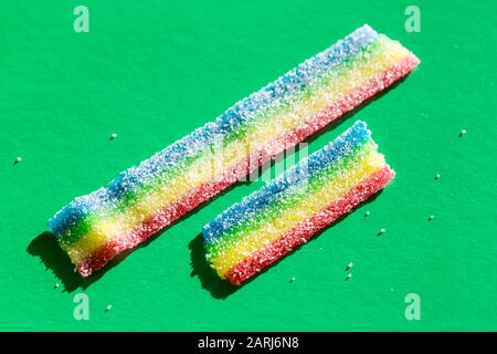 Varicolorierte Marmelade im Zucker auf dem grünen Hintergrund. Lange Marmeladenbonbons in Naturregenbogenfarbe. Kopierbereich, leere Vorlage für Text Stockfoto