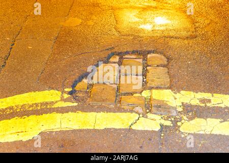 Ein zerbrochener Abschnitt der Asphalt Road Surface, enthüllt eine alte viktorianische gepflasterte Straße in Leeds. Stockfoto