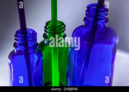 Drei kleine grüne und zwei blaue Flaschen mit Strohhalmen auf weißem und grauem Hintergrund Stockfoto