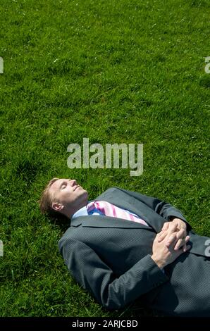 Entspannter Geschäftsmann, der an einem sonnigen Frühlingstag auf einem hellen grünen Rasenplatz liegt Stockfoto
