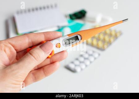 Weibliche Hand, die ein Digitalthermometer auf weißem Hintergrund mit Pillen hält. Kälte- und Grippekonzept. Stockfoto