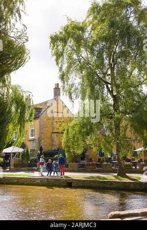 Eine Gruppe hoher Touristen neben dem seichten Fluss Windrush im Malerischen Bourton am Wasser im englischen Cotswolds UK Stockfoto