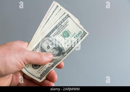 Hand hält Geld in US-Dollar auf grauem Hintergrund. Abbildung: Handhaltung von 100-Dollar-Scheinen. Geld in der Hand. Stockfoto