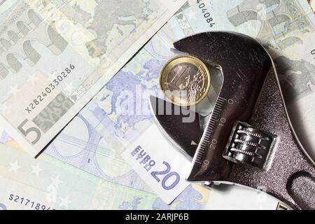 Eine Euro-Münze in einem verstellbaren Schraubenschlüssel auf verschiedenen Euro-Banknoten. Stockfoto