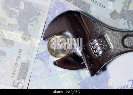 Eine Euro-Münze in einem verstellbaren Schraubenschlüssel auf verschiedenen Euro-Banknoten. Stockfoto